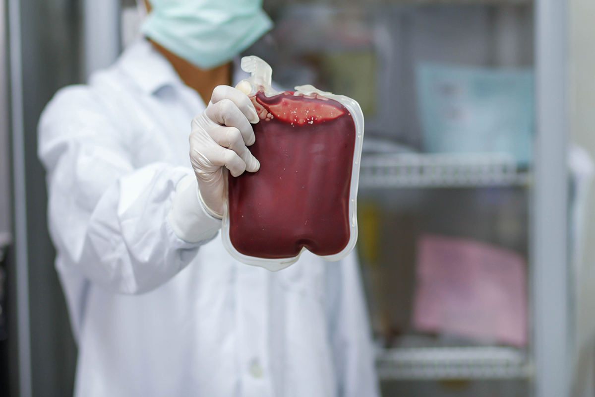 A person in a lab coat holding up a blood bag